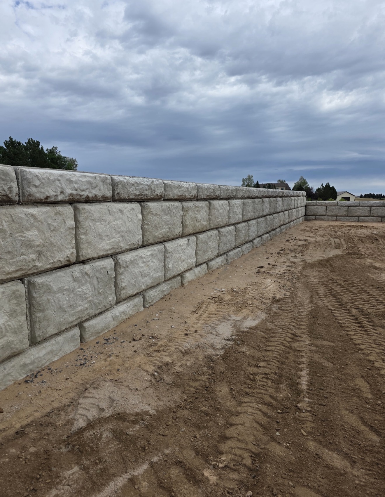 Long run of large-format boulder-style block retaining wall under a stormy Wyoming sky