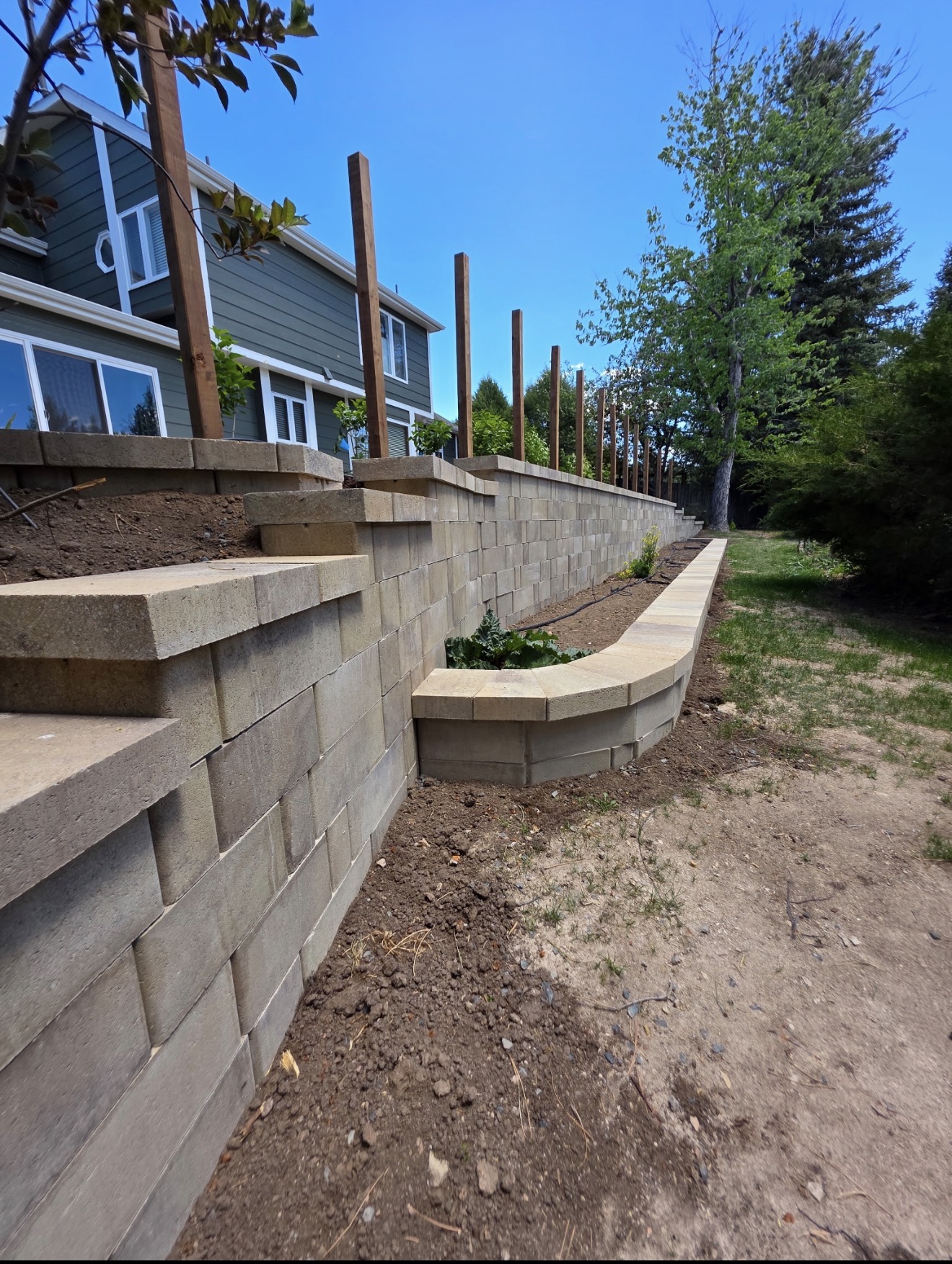 Curved modular-block retaining wall with built-in stone steps and a curved raised planter wall in a Cheyenne, Wyoming backyard